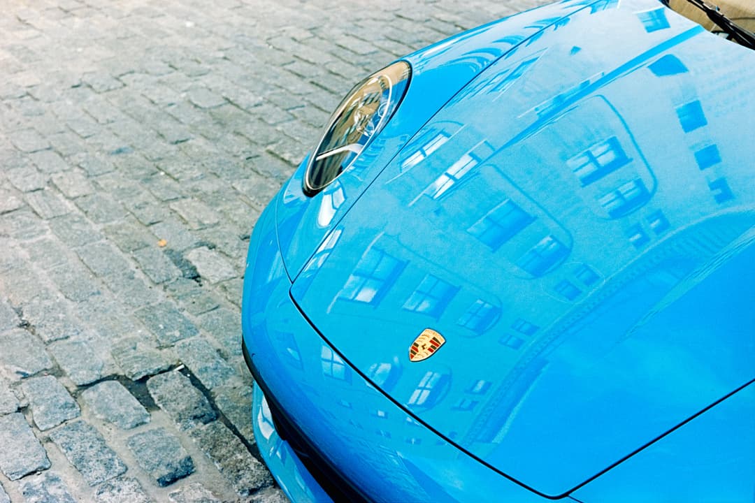 Close-up detail of bright blue Porsche hood on cobblestone street