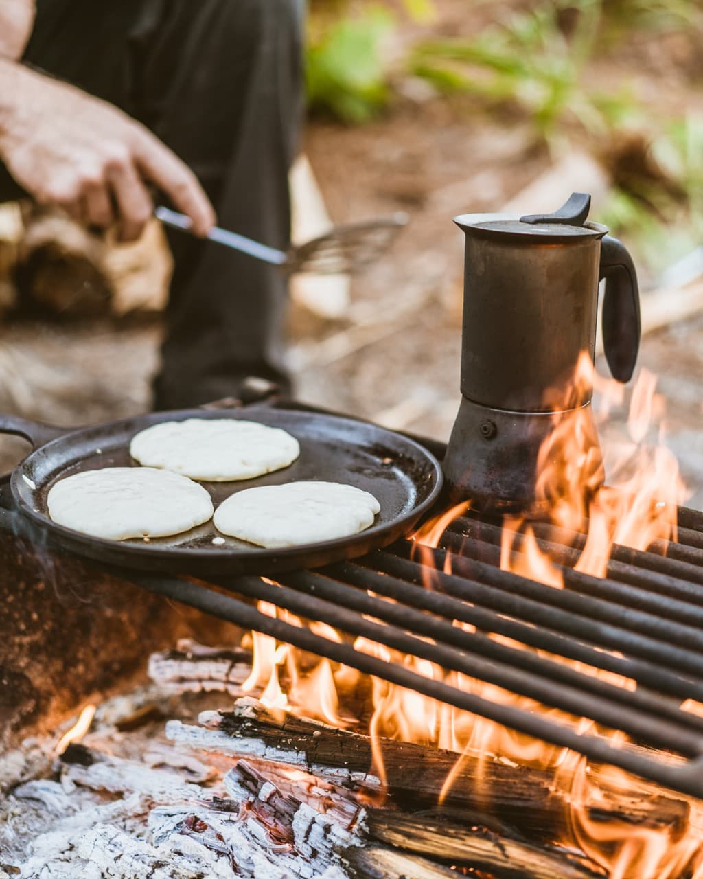 Campfire cooking scene with pancakes on griddle and coffee pot