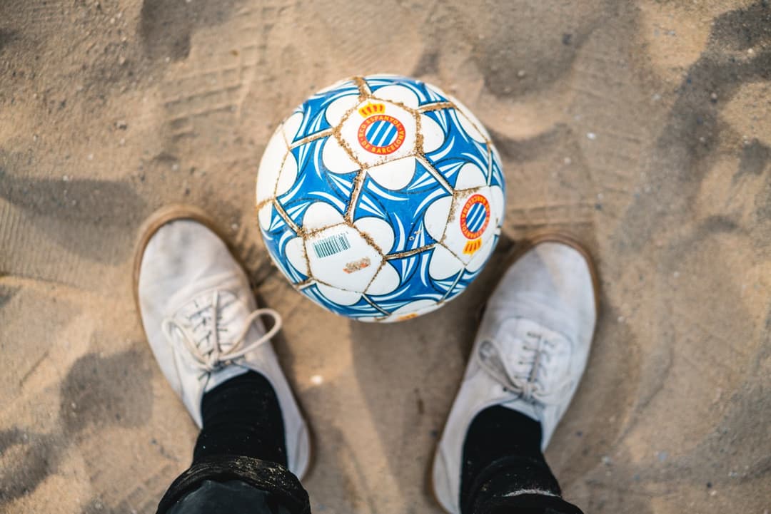 Soccer ball on a sandy beach with feet in sneakers, beach soccer game