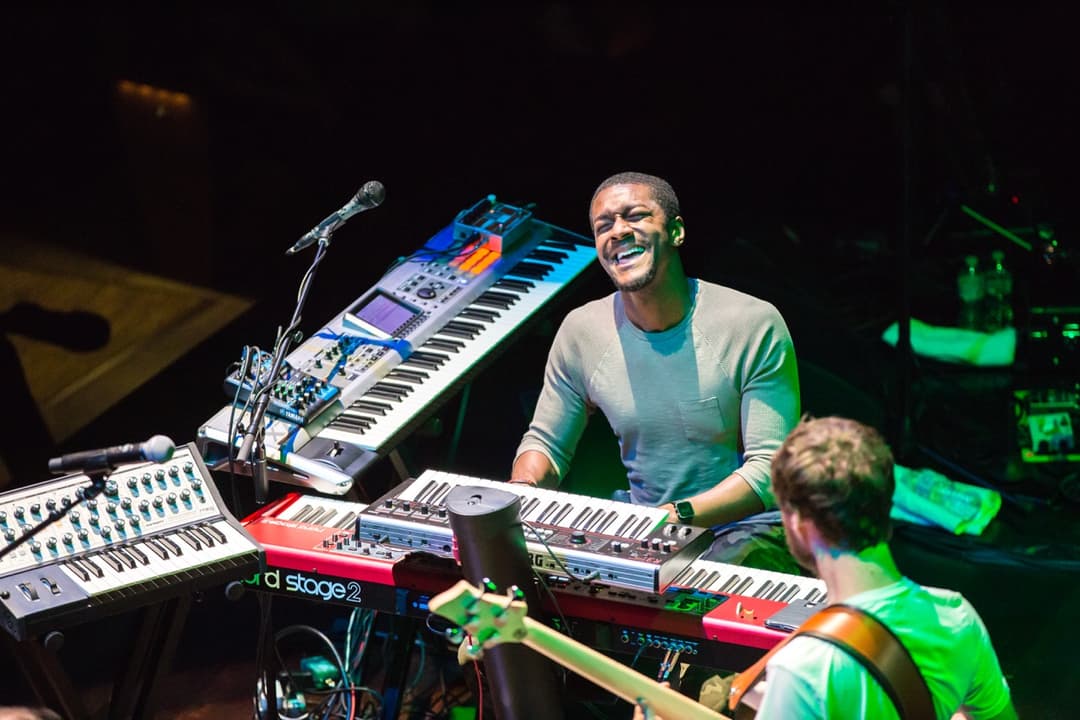 Live band performance: Multi-instrumentalist playing keyboards, bassist, and drummer on stage at concert