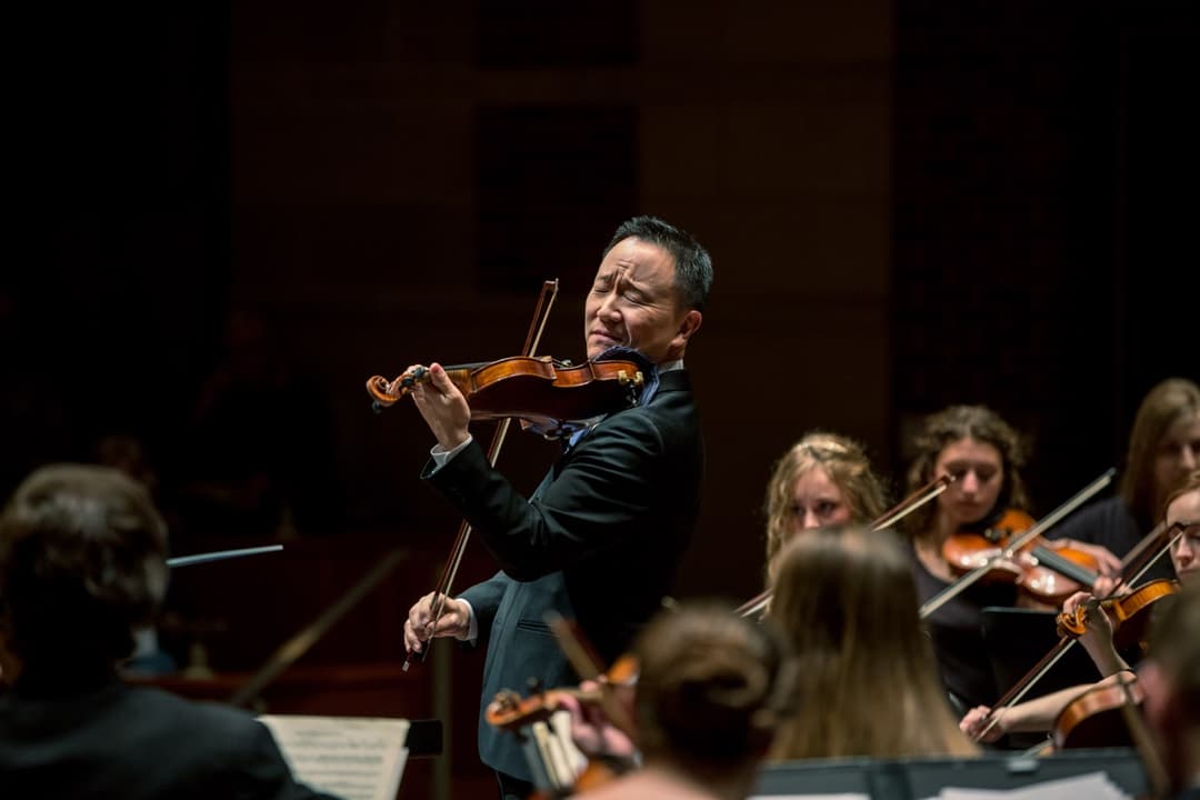 Orchestra performance: Conductor leading violinists and string instruments in concert hall