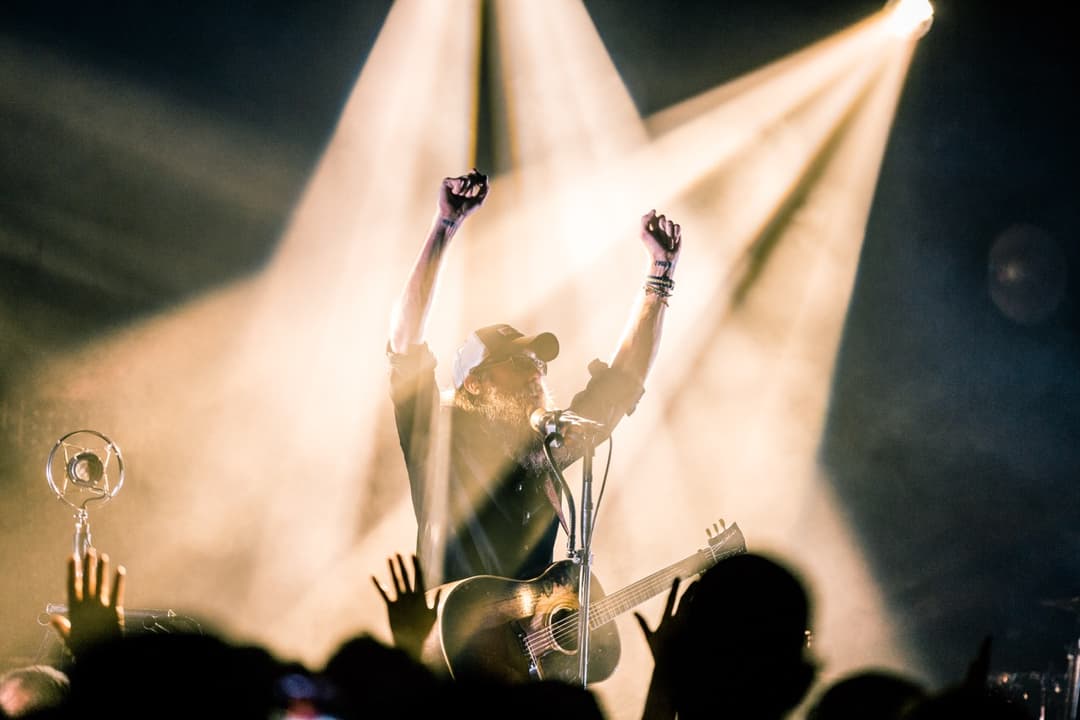 Concert photography: Musician with arms raised under bright stage lights at live music event