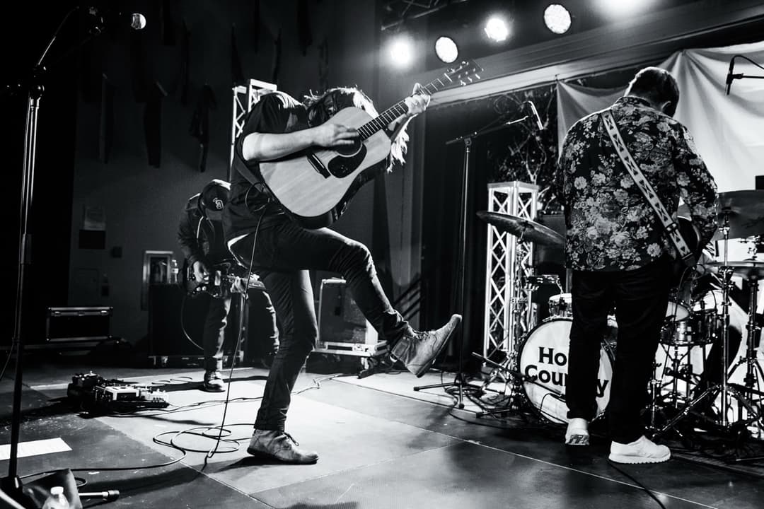 Black and white concert photography: Band performing on stage with guitarist, drummer, and stage lighting