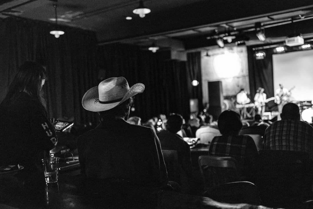 Black and white concert photography: Band performing in venue with audience and stage lighting