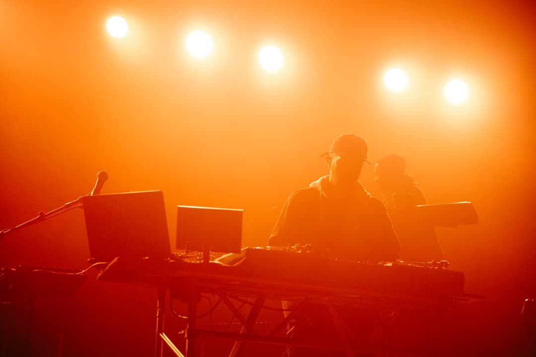 Live electronic music: Band performing on stage with orange stage lights and keyboardist