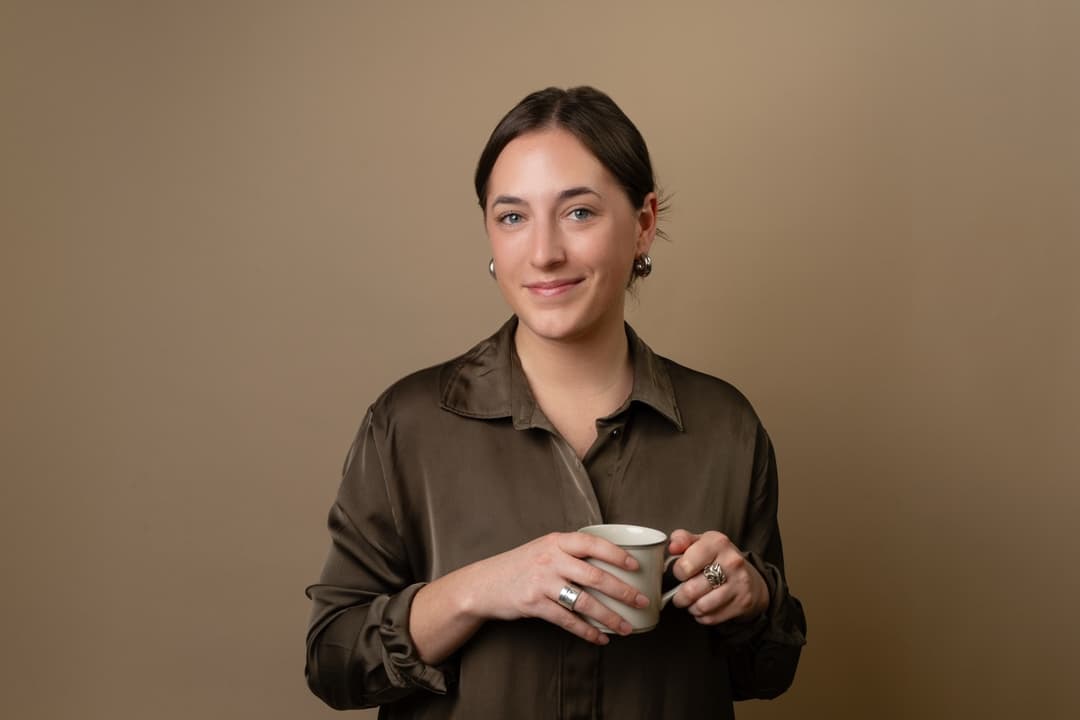 Professional headshot: Woman holding coffee cup with neutral background and natural lighting