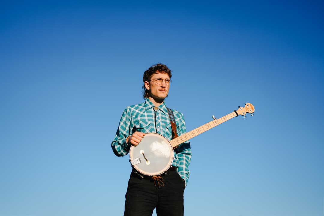 Musician portrait: Man playing banjo against blue sky in outdoor setting