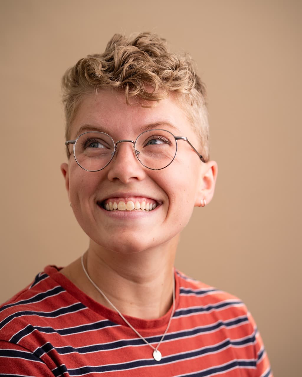 Portrait of smiling person: Non-binary individual with short hair and glasses in striped shirt