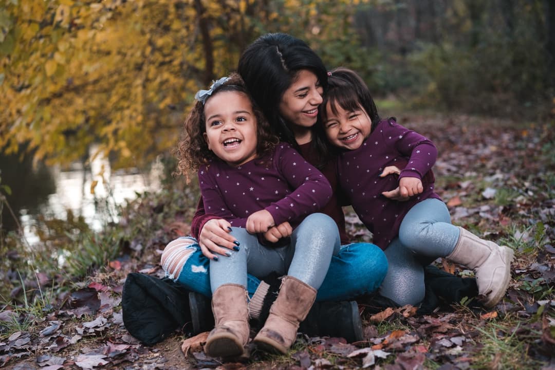 Children's portrait: Three young girls sitting together in outdoor setting with autumn leaves