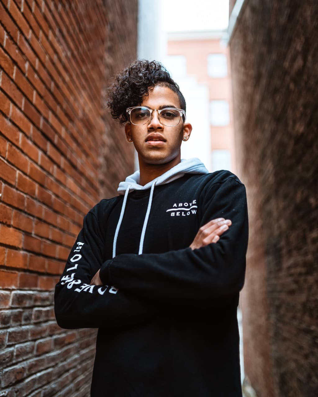 Urban portrait: Young man with curly hair and glasses in front of brick wall