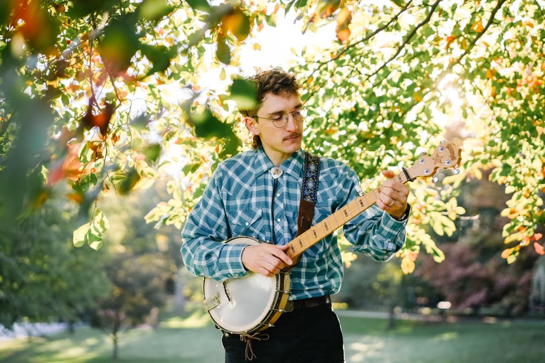 Outdoor portrait: Musician playing banjo in park with natural lighting and foliage