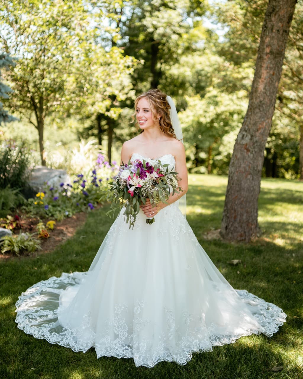 Bride in a white lace wedding dress holding a bouquet, outdoor wedding portrait