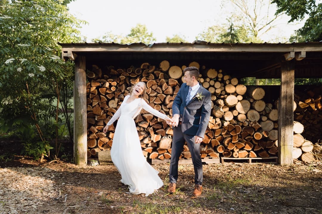 Bride and groom posing in front of a wood pile, rustic wedding photography