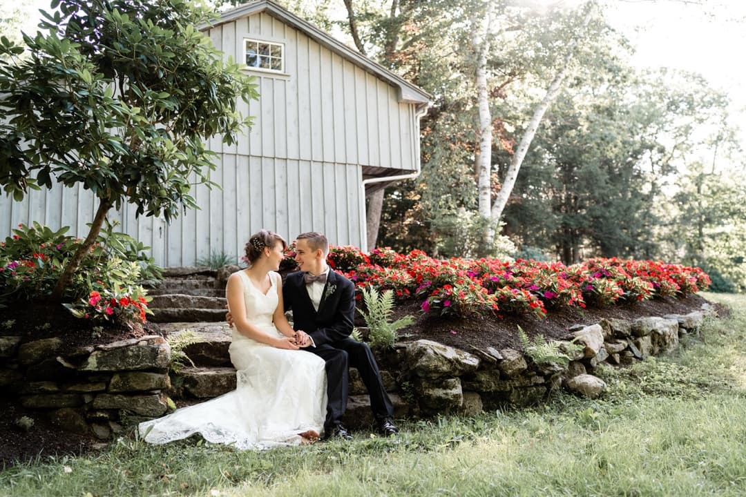 Bride and groom sitting on a stone wall with red flowers, outdoor wedding portrait