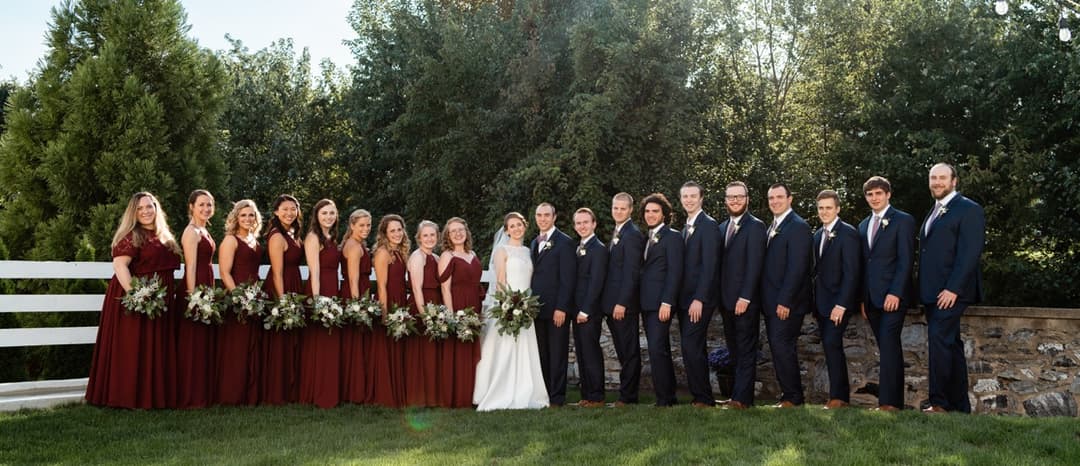 Wedding party posing in maroon dresses and navy suits, group wedding photo