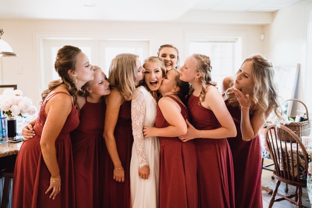 Bridesmaids hugging the bride in maroon dresses, wedding party photo