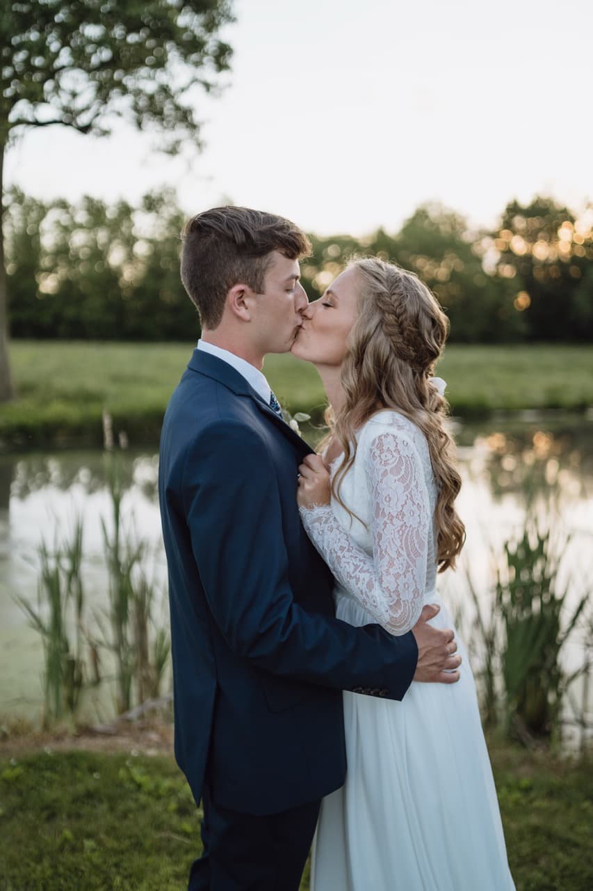 Bride and groom kissing by a pond, romantic wedding moment