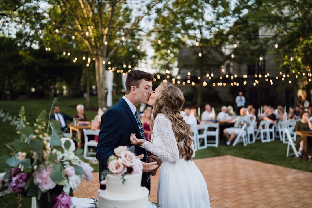 Bride and groom cutting the wedding cake under string lights, outdoor wedding reception