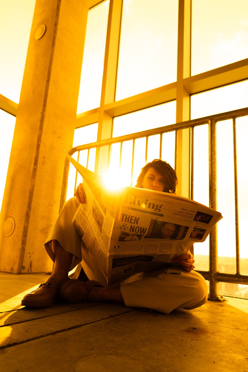 Model sitting on floor reading newspaper in golden hour light